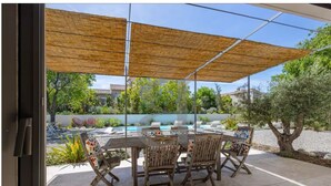 An outdoor patio with a table and chairs, a pool in the background, and a shaded area with a view of the surrounding landscape. - House at the foot of the Alpilles (Saint-Rémy-de-Provence)