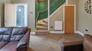 A living room with a brown leather sofa, a wooden floor, a staircase with green walls, and a wooden door. - UK47330 - Olive Cottage (Amble)