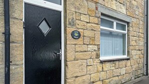 A stone building with a black door and a window with white shutters. - UK47330 - Olive Cottage (Amble)