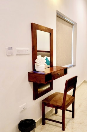 A wooden desk with a mirror and a chair, a window with a blind, and a trash can. - Radha Kunj Resort (Pushkar)