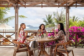 A group of people dining at an outdoor table with a view of the ocean and palm trees. - Eliana Resort and Spa (Rote Ndao Regency)