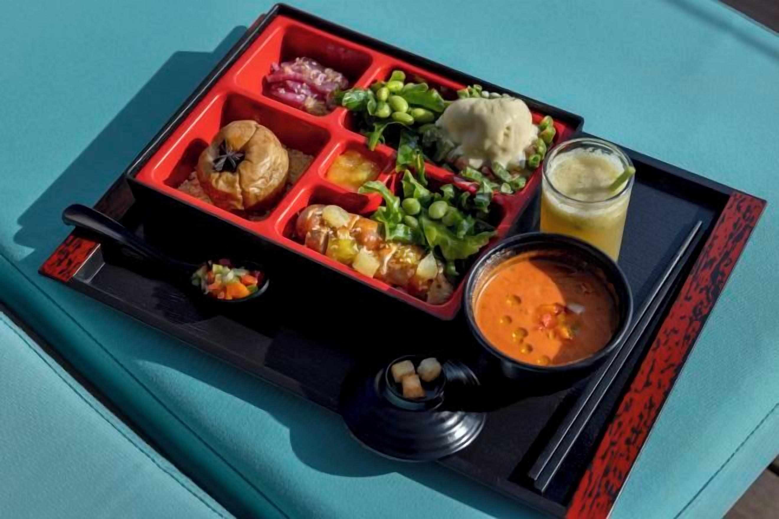 A tray with a variety of food items including a bowl of soup, a glass of juice, and several compartments with different foods.