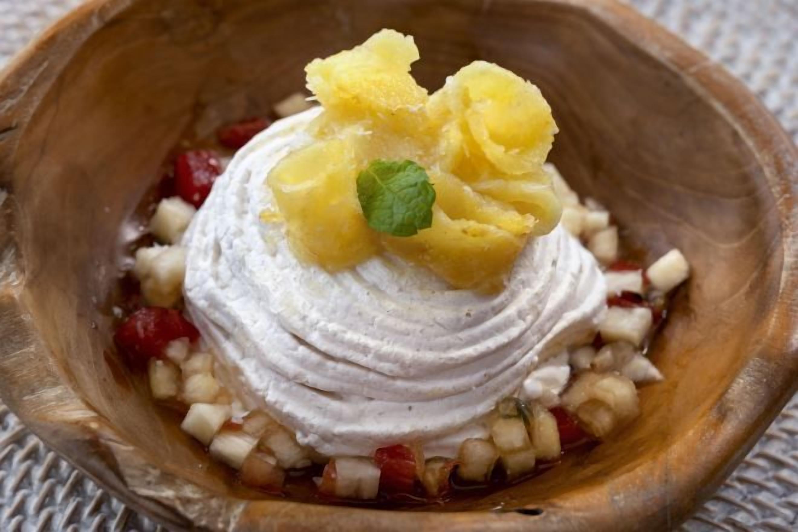 Un postre en un cuenco de madera con crema batida y guarnición de fruta.