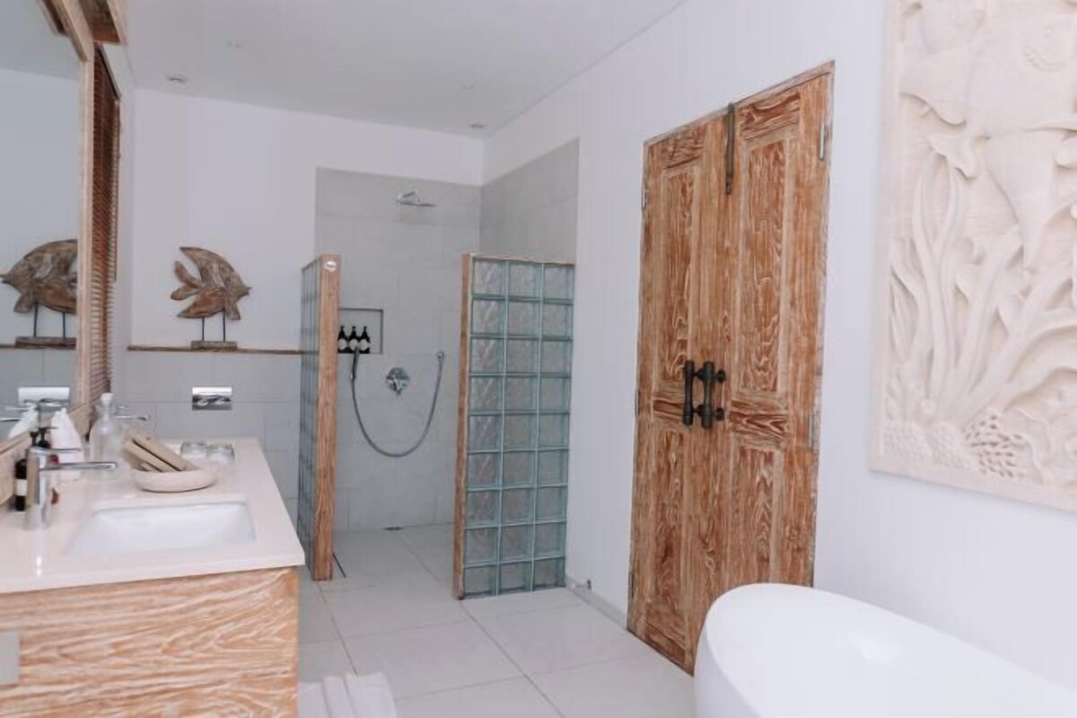 Un baño moderno con puerta de madera, cabina de ducha de vidrio e lavamanos de mármol.