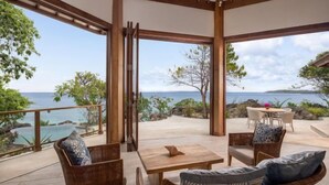 Un vaste espace extérieur aménagé avec des meubles en osier, une table en bois et une vue sur l’océan.