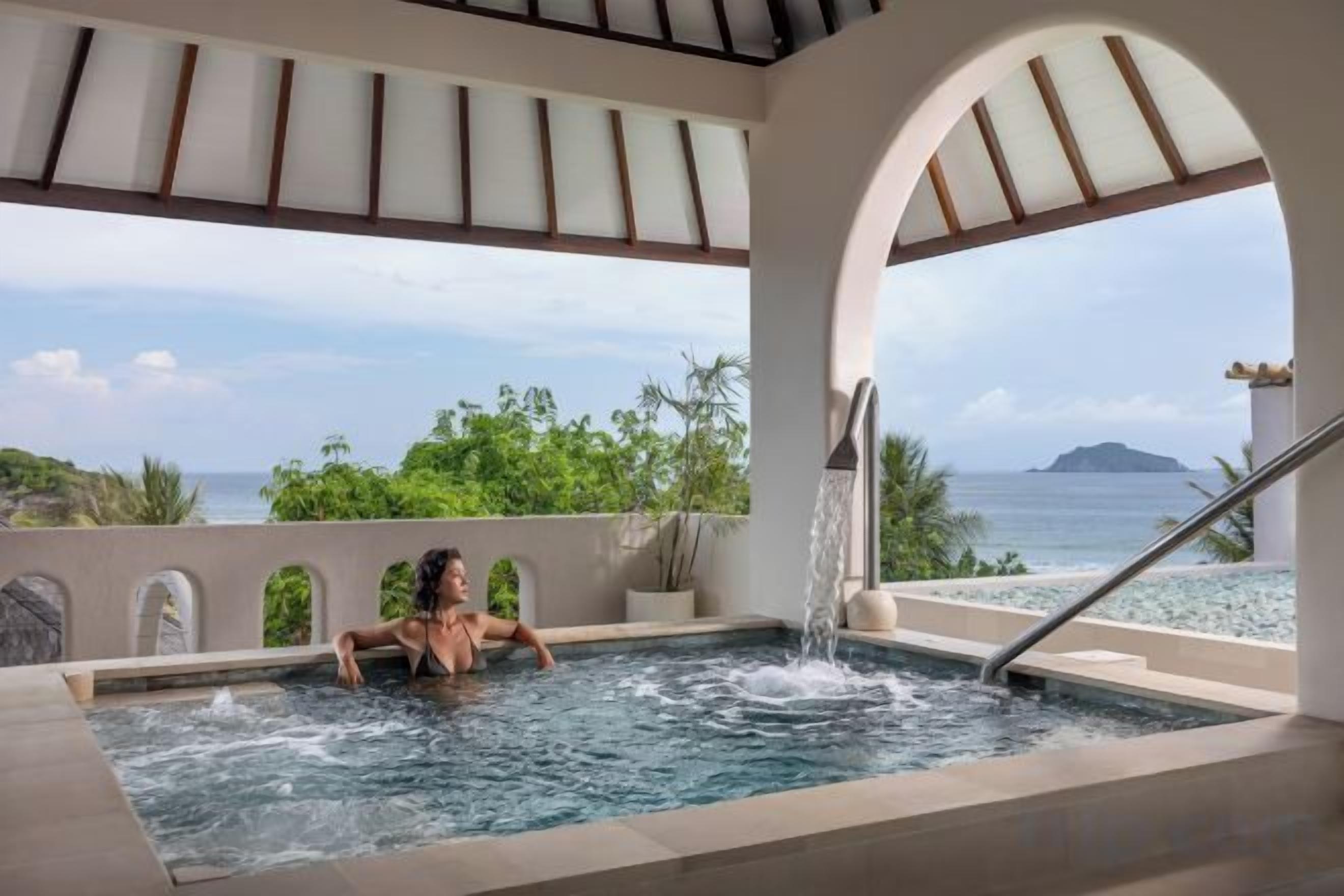 A person in a hot tub with a view of the sea and greenery.