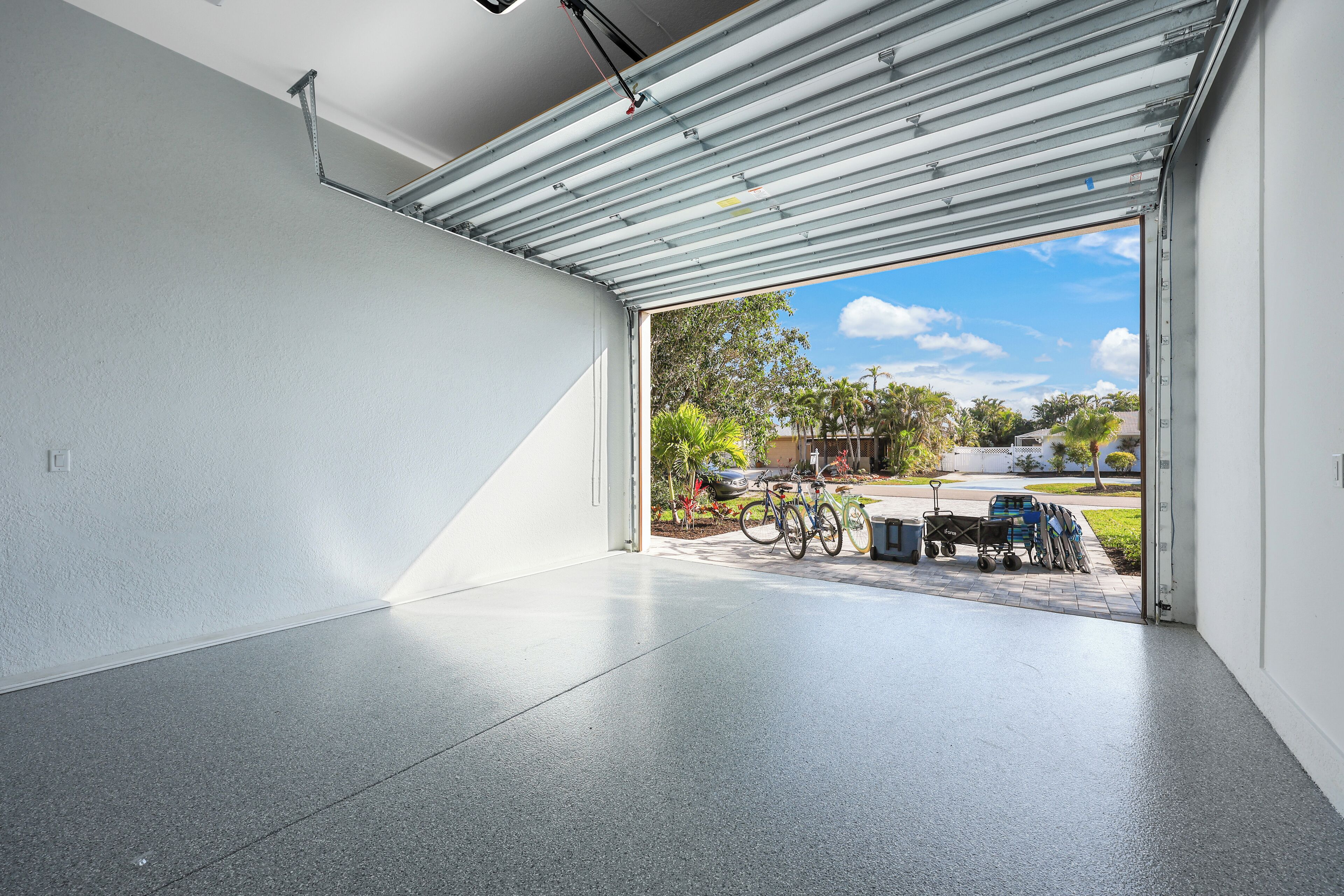 A garage with a metal door open, revealing bicycles and a cart outside.