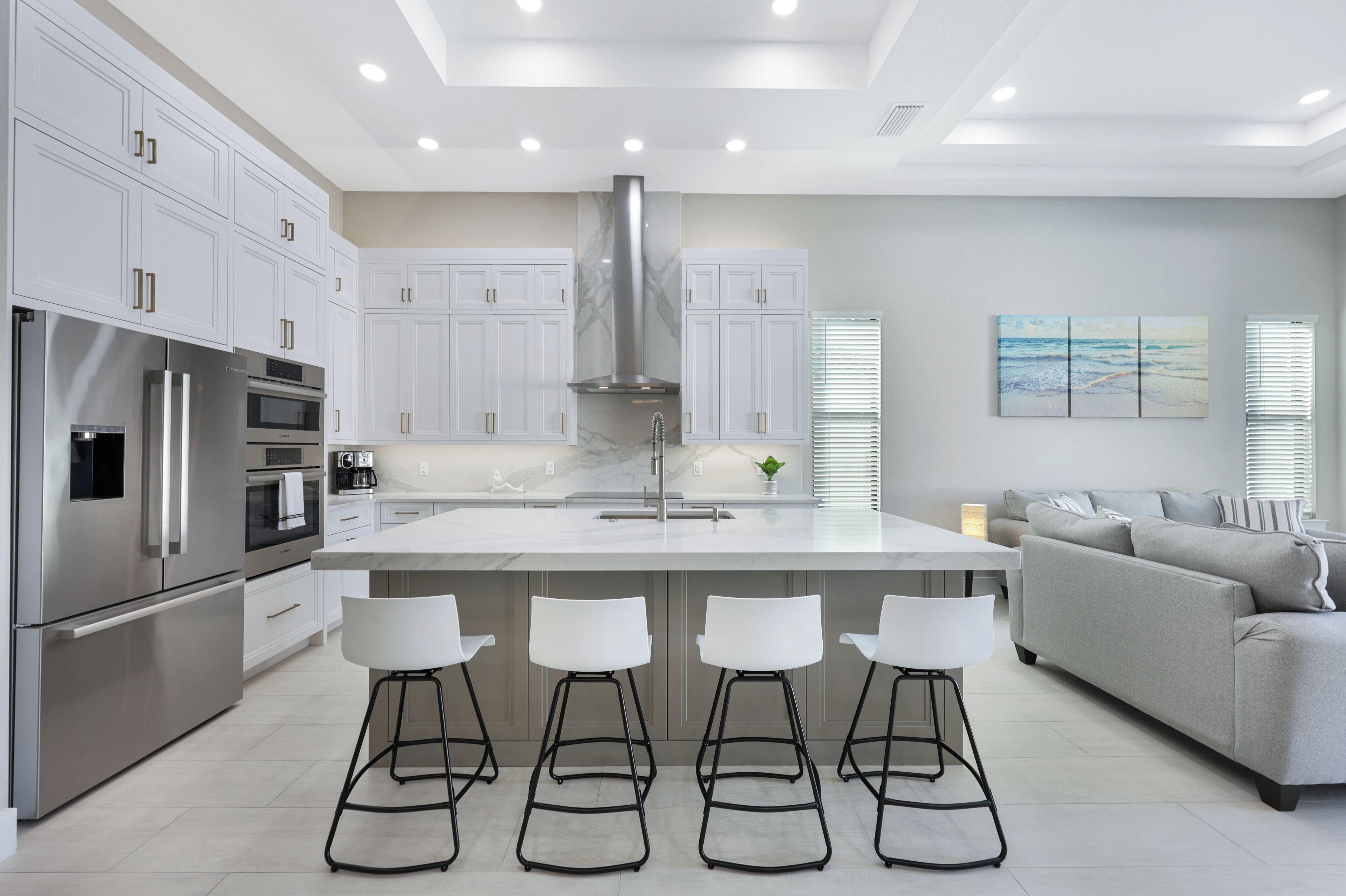 Una cocina moderna con armarios blancos, electrodomésticos de acero inoxidable y una isla central con taburetes de bar.