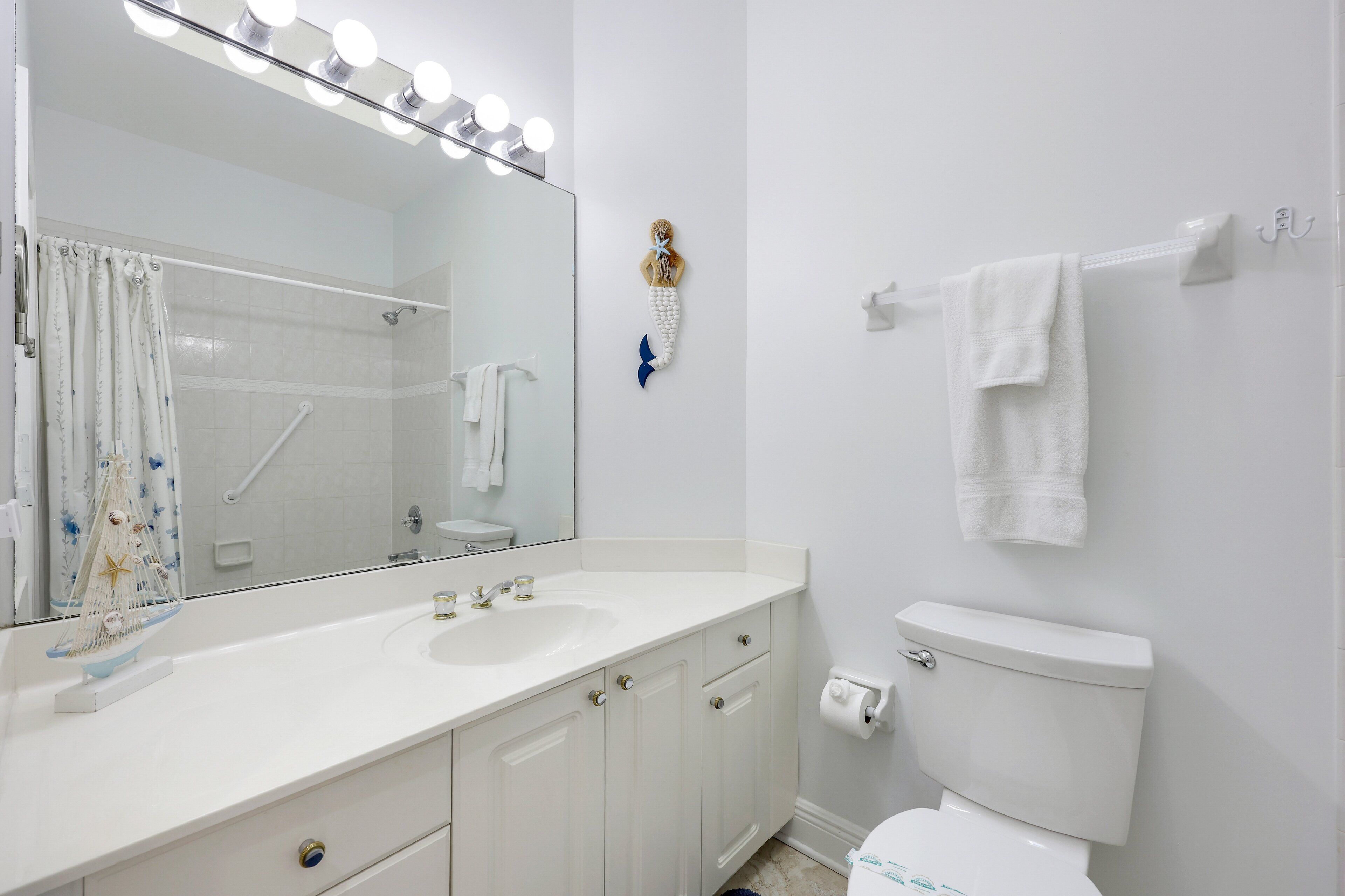 Un bagno con lavandino bianco, specchio e water. Ci sono luci sopra lo specchio e un porta asciugamani a parete.