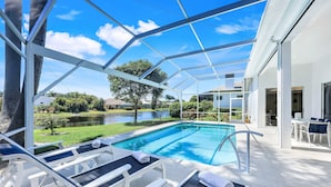 A covered outdoor swimming pool with lounge chairs and a view of a lake and greenery.