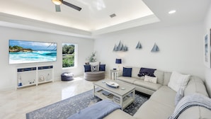 A modern living room with a flat-screen TV, a ceiling fan, and nautical decor.
