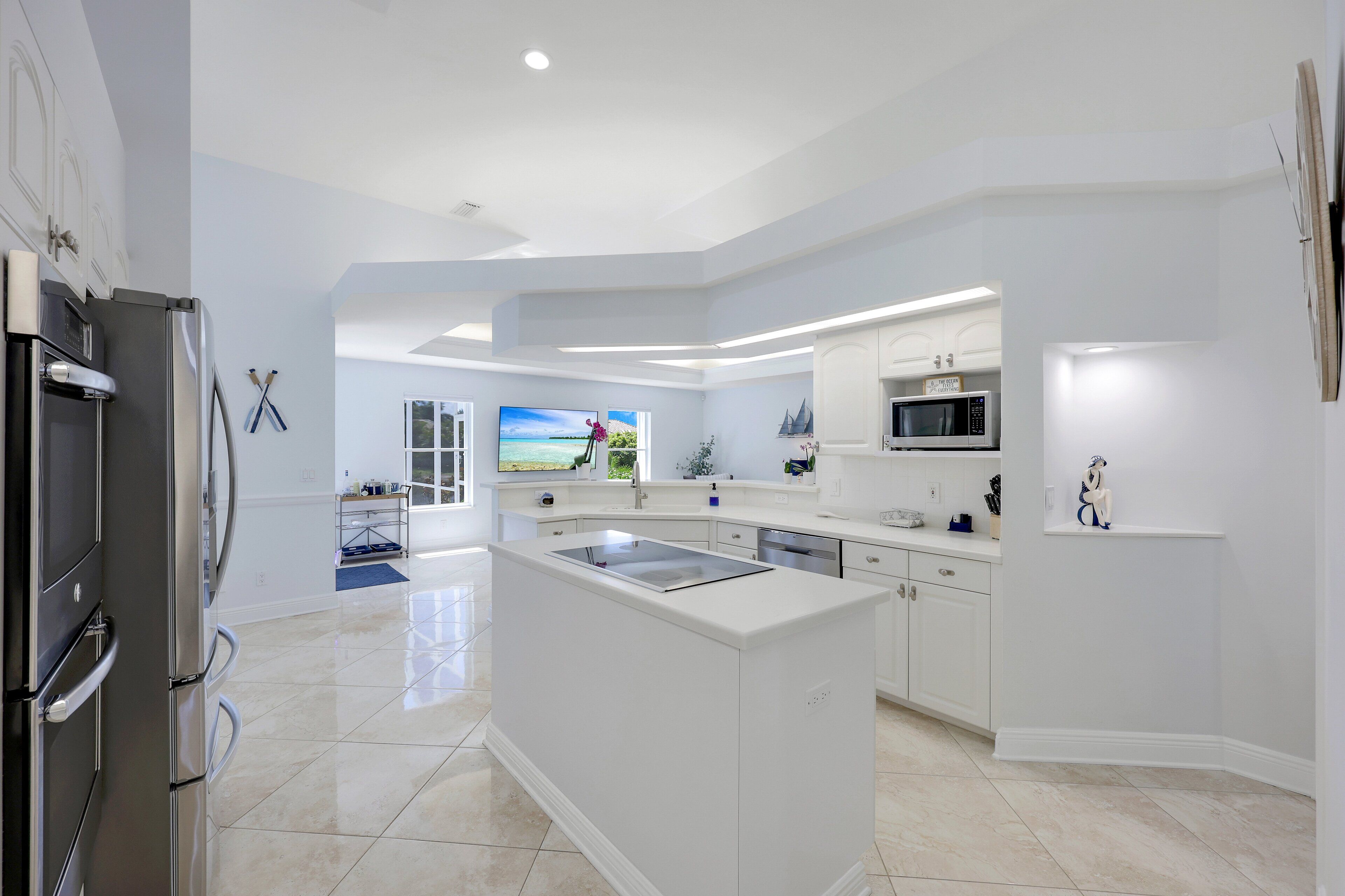 A modern kitchen with white cabinetry, a central island, and a large window with a view of the outdoors.