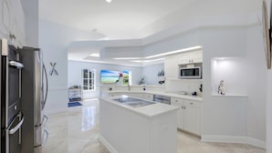 A modern kitchen with white cabinetry, a central island, and a large window with a view of the outdoors.