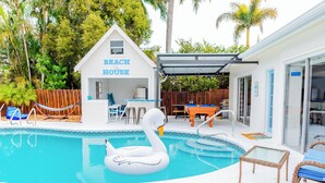 A swimming pool with a swan float, a covered patio, and a house labeled "Beach House". - New! Fun in the Sun - Beautifully Renovated! Heated Pool - Pool Table! (Naples)