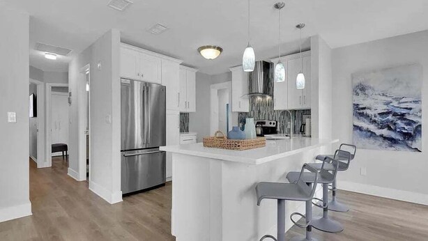 A modern kitchen with stainless steel appliances, a central island with bar stools, and a large abstract painting on the wall. - New! Fun in the Sun - Beautifully Renovated! Heated Pool - Pool Table! (Naples)