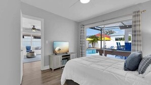 A bedroom with a bed, a TV, a ceiling fan, and a view of an outdoor pool area. - New! Fun in the Sun - Beautifully Renovated! Heated Pool - Pool Table! (Naples)