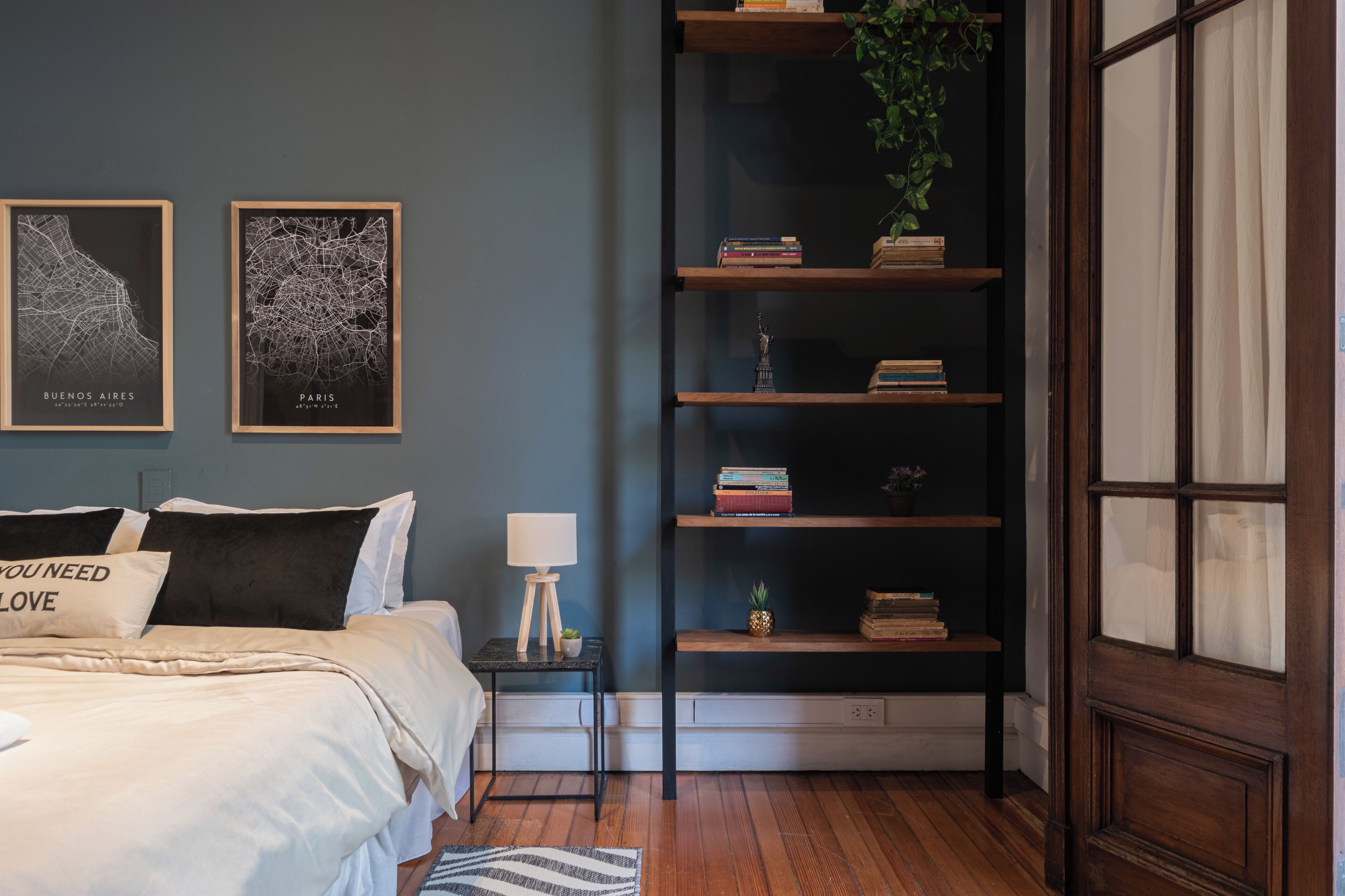 Ein Schlafzimmer mit einem Bett, einem Nachttisch, einem Bücherregal und zwei gerahmten Karten.