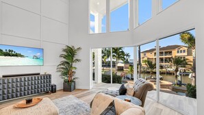 A spacious living room with a large TV, comfortable seating, and a view of a waterfront property. - Tropical Oasis! - Luxury Canal Home! 1 Mile To The Beach! Heated Pool & Spa (Naples)