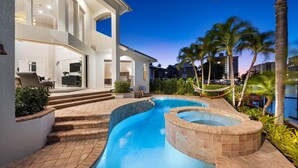 A modern house with a swimming pool, outdoor seating, and a view of palm trees. - Tropical Oasis! - Luxury Canal Home! 1 Mile To The Beach! Heated Pool & Spa (Naples)