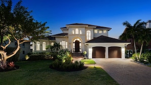 A two-story house with a central entrance, a covered driveway, and a well-maintained lawn. - Tropical Oasis! - Luxury Canal Home! 1 Mile To The Beach! Heated Pool & Spa (Naples)