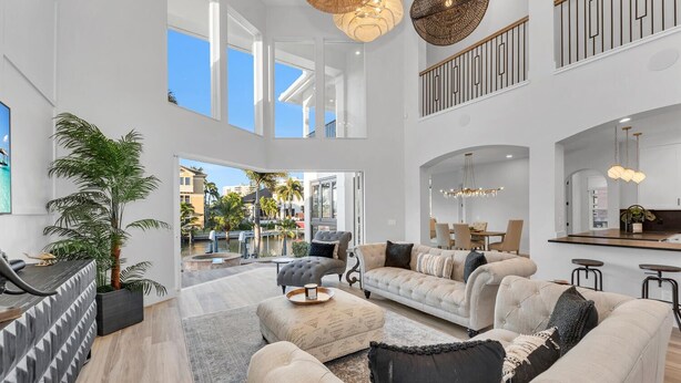 A spacious living room with a large sofa set, a coffee table, and a dining area with a high ceiling and large windows. - Tropical Oasis! - Luxury Canal Home! 1 Mile To The Beach! Heated Pool & Spa (Naples)