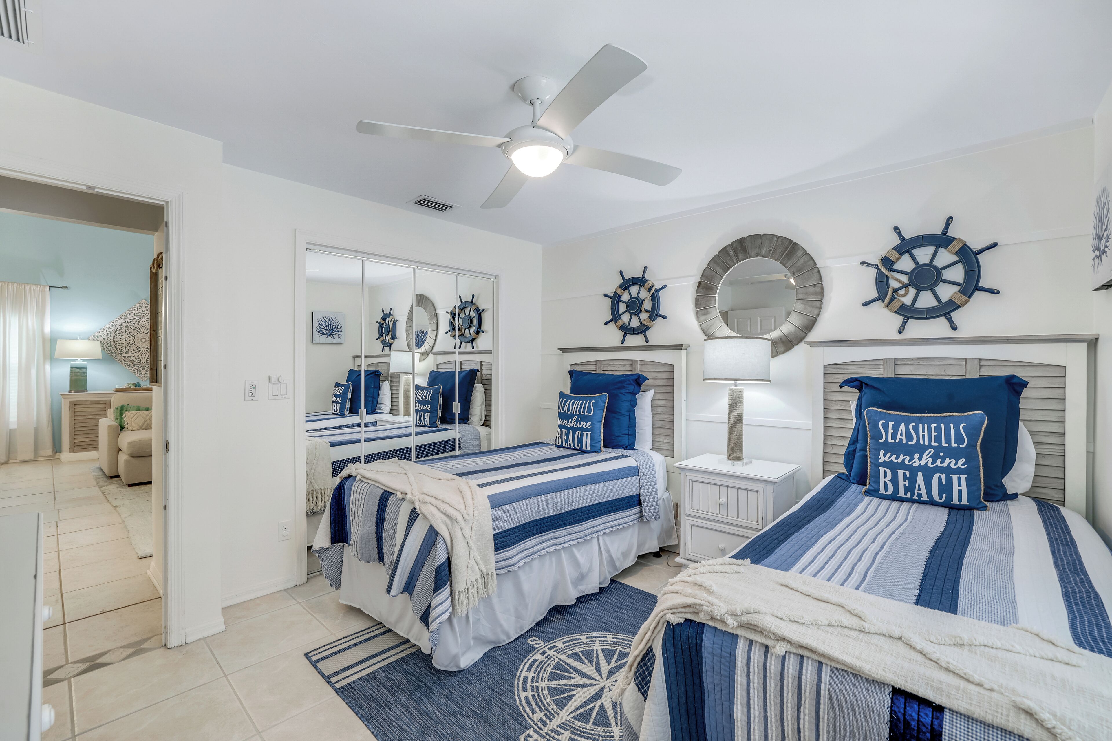 A bedroom with two beds, nautical-themed decor, and a ceiling fan.