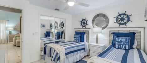 A bedroom with two beds, nautical-themed decor, and a ceiling fan.