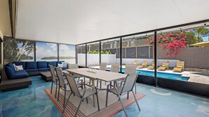 A modern outdoor living area with a pool, seating, and large windows. - Sea La Vie - Pickleball close by, Heated Pool, Walk to Beach! (Naples)