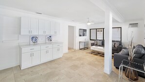 A spacious living area with a white kitchen, grey sofa, and a coffee table. - Sea La Vie - Pickleball close by, Heated Pool, Walk to Beach! (Naples)