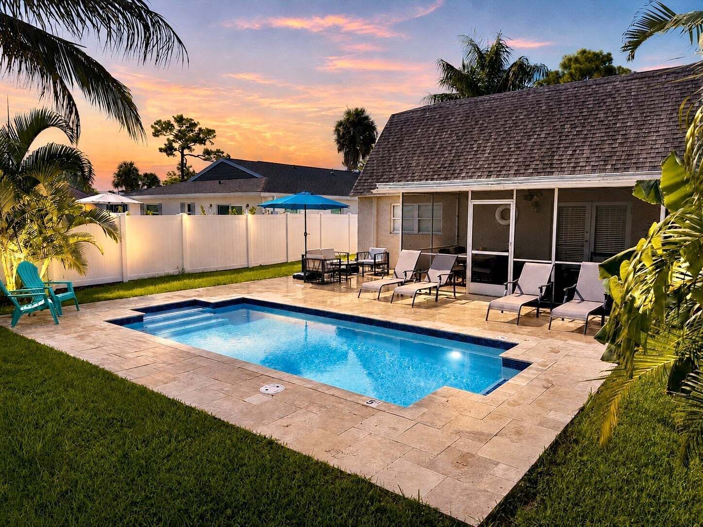 A backyard with a swimming pool, patio furniture, and a white fence.