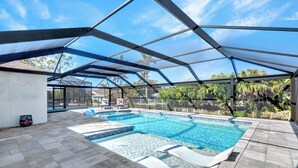 An outdoor swimming pool with a glass enclosure, surrounded by a patio area with stone tiles.