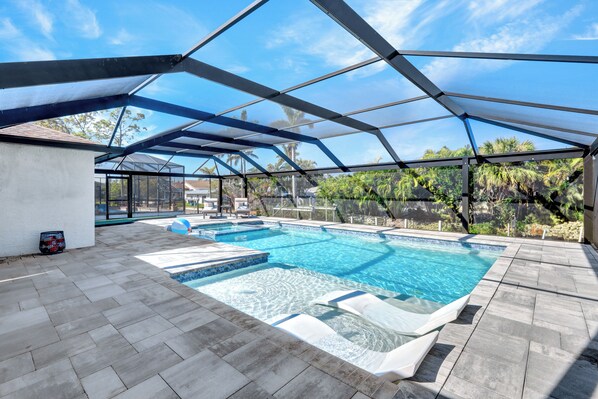Una piscina exterior con cerramiento de vidrio, rodeada por un patio con baldosas de piedra.