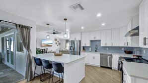A modern kitchen with white cabinets, a central island with bar stools, stainless steel appliances, and a view to a balcony.