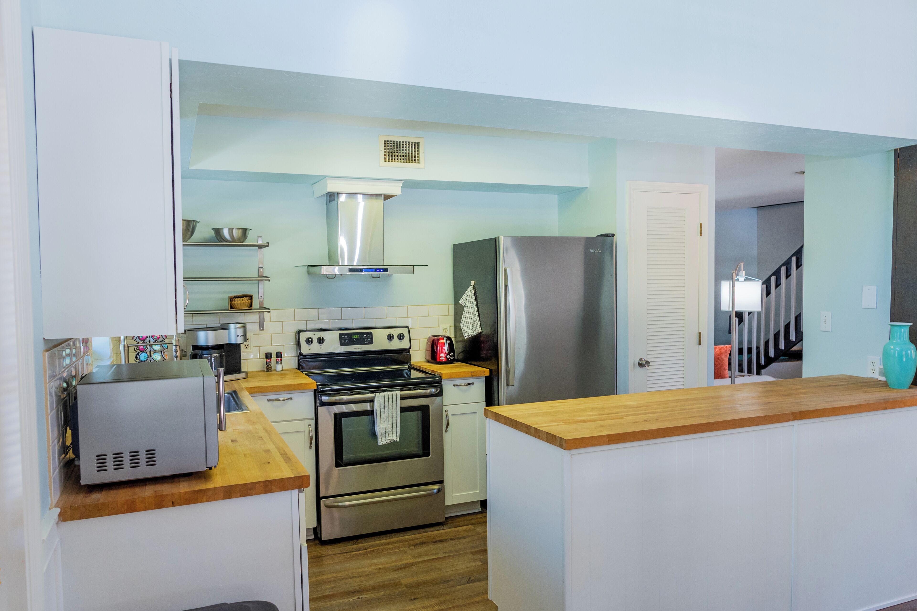 A compact kitchen with white cabinets, stainless steel appliances, and a wooden countertop.