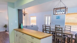 A modern kitchen with white cabinets, a wooden countertop, and a dining area with wooden chairs and a table.