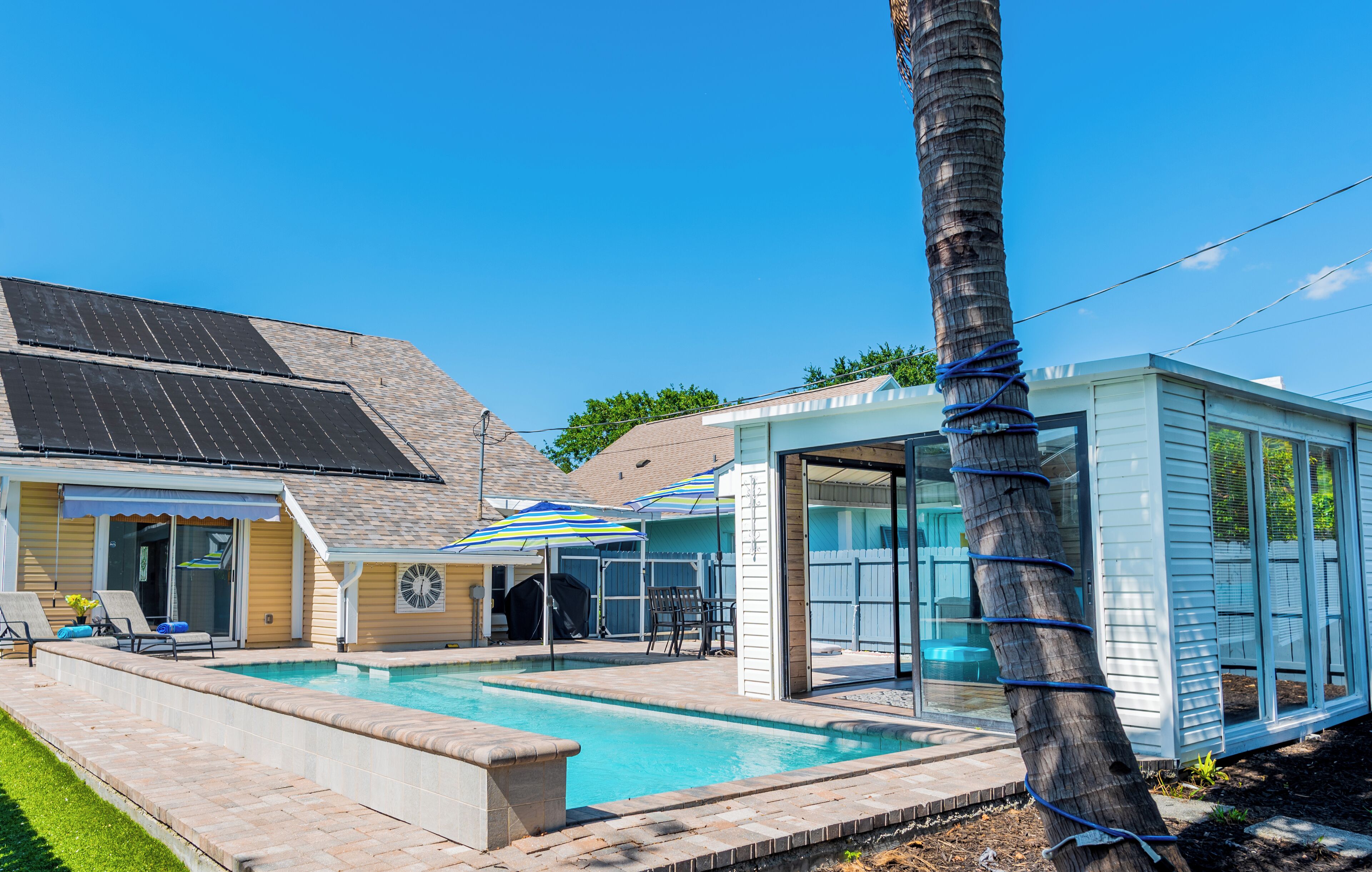 Een achtertuin met een zwembad, een overdekt terras en een huis met zonnepanelen op het dak.