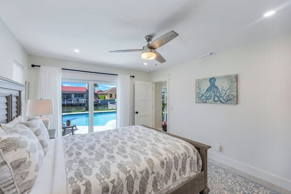 A bedroom with a bed, a ceiling fan, a painting, and a view of a pool and outdoor seating. - Sunny Side! – Southern Exposure - Heated Saltwater Pool! Walk to Beach! (Naples)