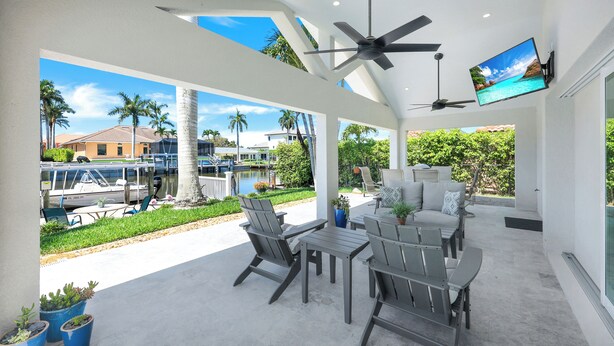 A covered patio with outdoor furniture, a ceiling fan, and a TV screen. - Sunny Side! – Southern Exposure - Heated Saltwater Pool! Walk to Beach! (Naples)