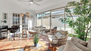 A sunlit room with a ceiling fan, wicker furniture, a desk, and a large sliding glass door leading outside.
