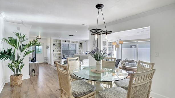 A dining area with a glass table surrounded by wicker chairs, a potted plant, and a modern pendant light.
