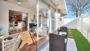 A patio with wicker furniture, a glass door leading to a kitchen, and a white fence.