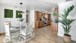A modern kitchen with wooden cabinets, a central island, and a dining area with white wicker chairs.