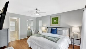 A bedroom with a bed, bedside tables, a ceiling fan, and a door leading to another room.