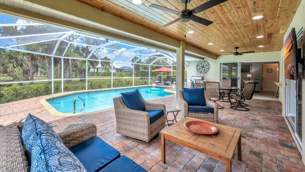 A covered outdoor area with a pool, wicker furniture, and a wooden ceiling.
