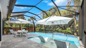A swimming pool with white lounge chairs and umbrellas, surrounded by a glass enclosure and palm trees.