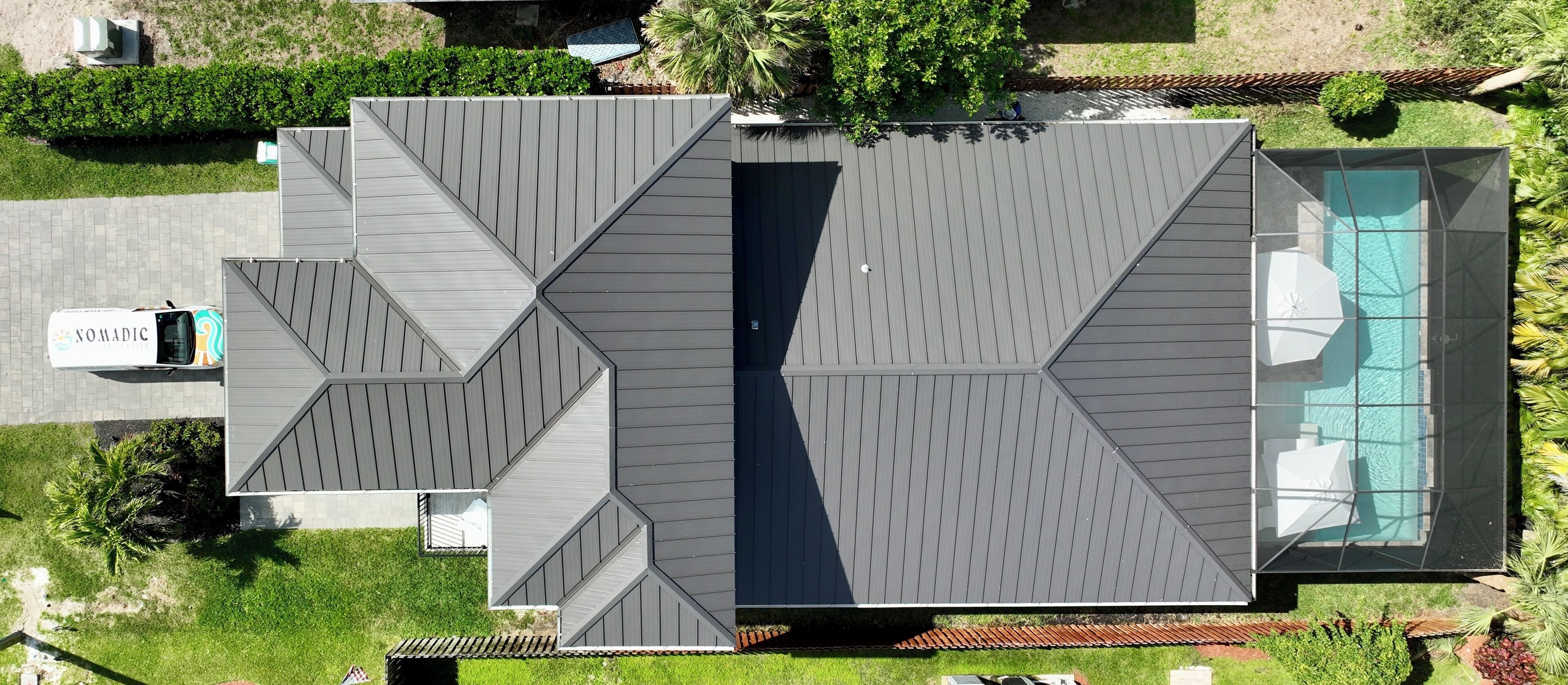Ein modernes Haus mit einem einzigartigen, geometrischen Dach, einem Schwimmbad und einem gepflegten Rasen.