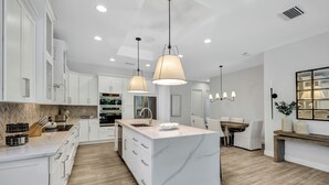 A modern kitchen with white cabinetry, a marble island, and pendant lighting.