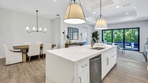 A modern kitchen with a large island, white cabinetry, and pendant lighting.