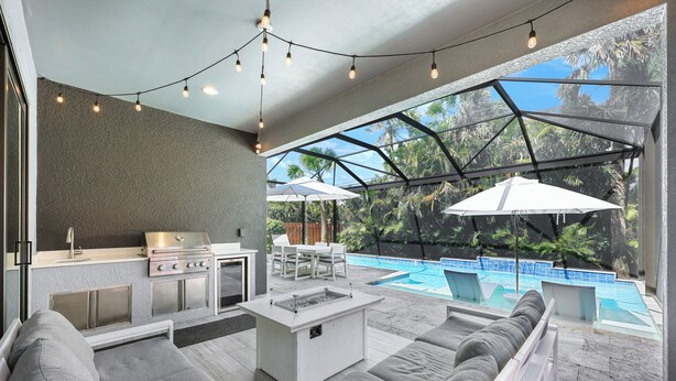 A modern outdoor kitchen with a grill, dining area, and a poolside seating area with umbrellas.