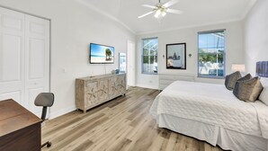 A bedroom with a large bed, a ceiling fan, a wooden dresser, and a television on the wall. - New! Sunkissed - 1 Mile to Beach! Heated Pool! (Naples)